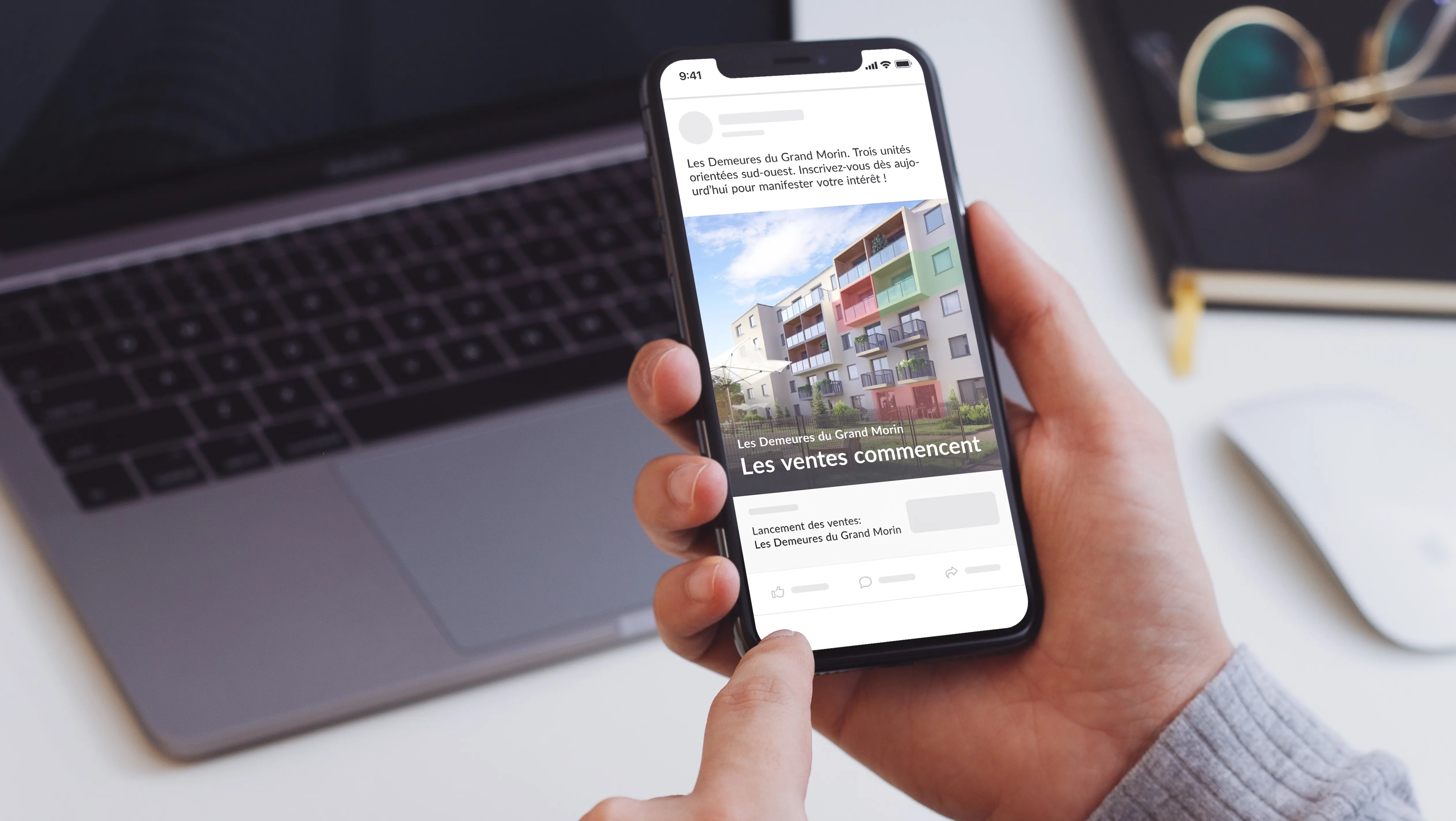 Une personne tient un smartphone affichant une annonce immobilière pour « Les Demeures du Grand Morin ». Le message indique que trois unités orientées sud-ouest sont disponibles, avec un visuel du bâtiment et le texte « Les ventes commencent ».